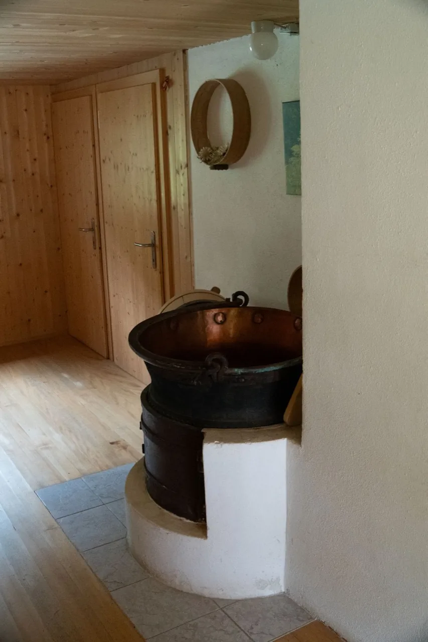 Derselbe Kupferkessel vom Flur aus gesehen, mit Nietreihe unter dem Rand und geschmiedetem Griff, an der Wand ein großer Holzreif mit getrockneten Silberdisteln