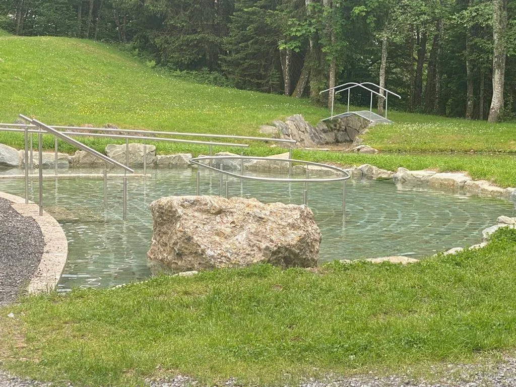 Klares, grünlich schimmerndes Wasser im Tretbecken der Kneippanlage, ein heller Felsblock in der Mitte, Edelstahlgeländer zum Festhalten