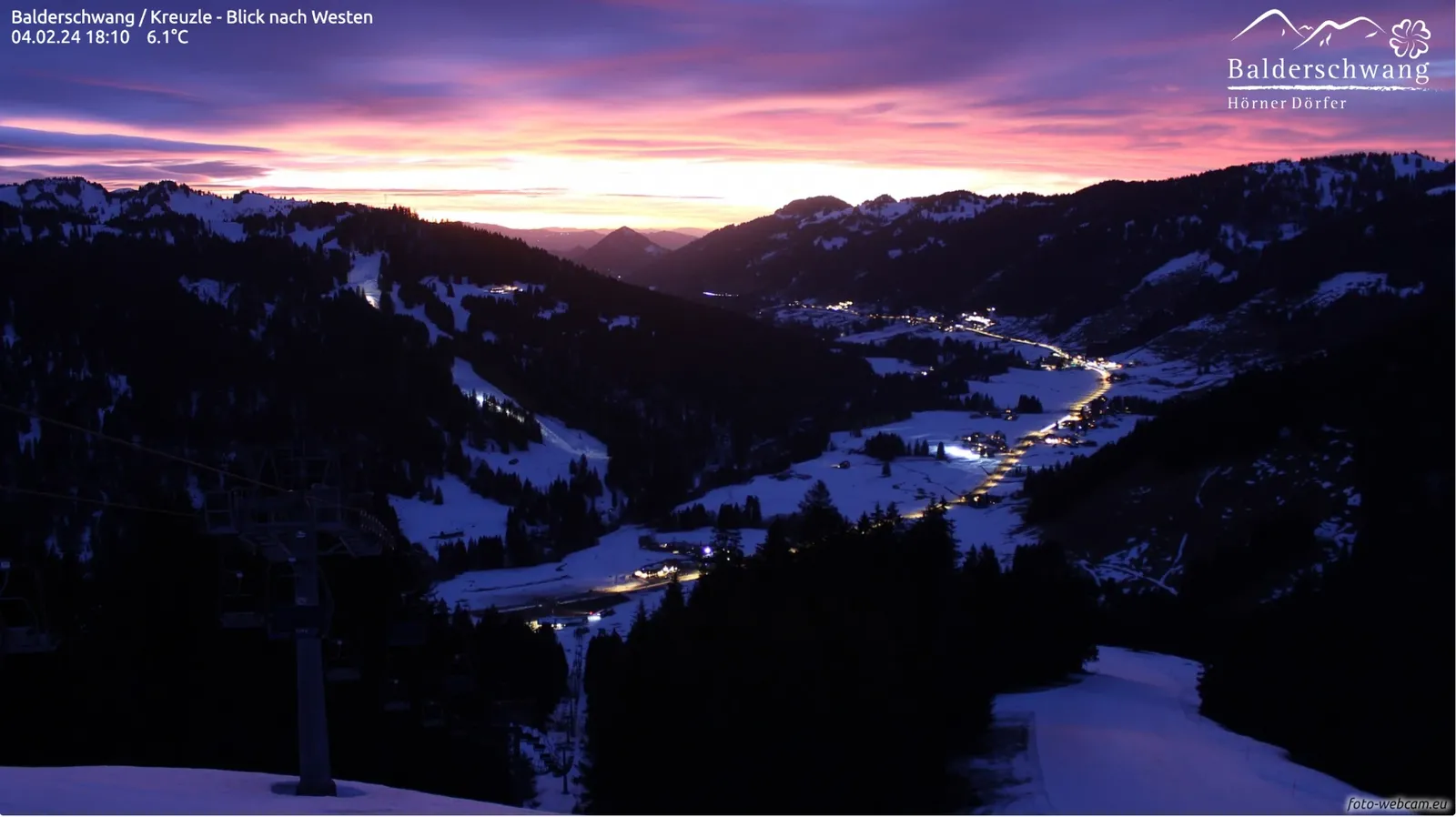 Violetter und rosa Abendhimmel über dem verschneiten Tal, das in blaues Dämmerlicht getaucht ist