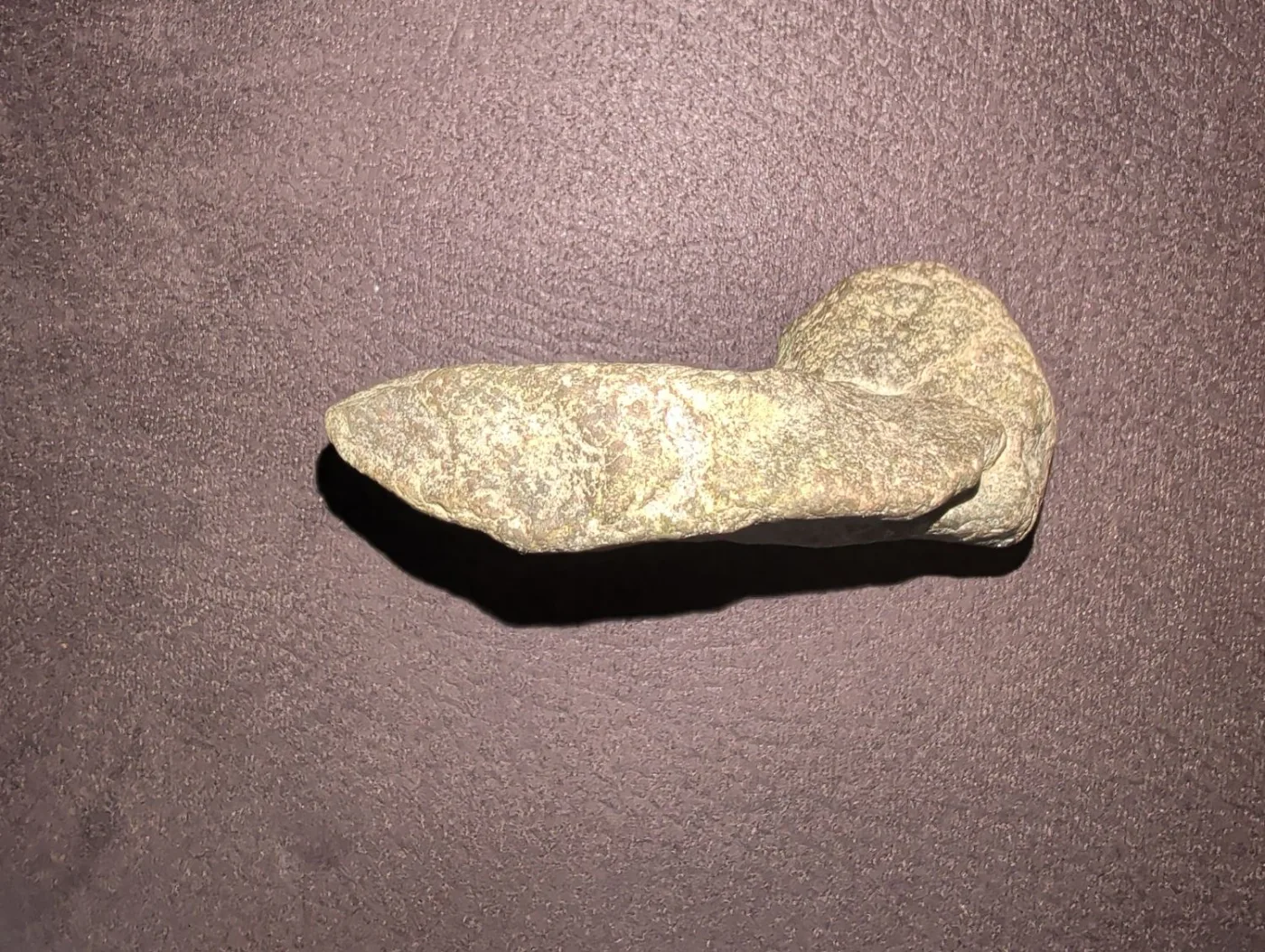 Grünlich-graue Steinaxt auf dunklem Stoff, von oben fotografiert, mit hartem Schlagschatten an der Unterkante